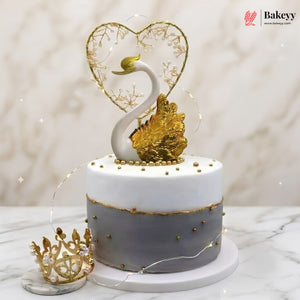Decorative cake with swan and heart design on a marble surface, featuring the Bakeyy brand.