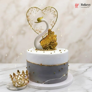 Decorative cake with swan and heart design on a marble surface, featuring the Bakeyy brand.