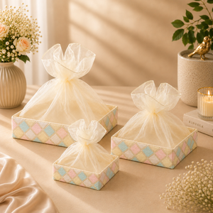 Three decorative boxes with pastel checkered pattern and sheer white bows on a soft beige surface.