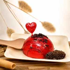 Red jelly dessert with a heart on top on a white plate with a wooden spoon, surrounded by dried plants.