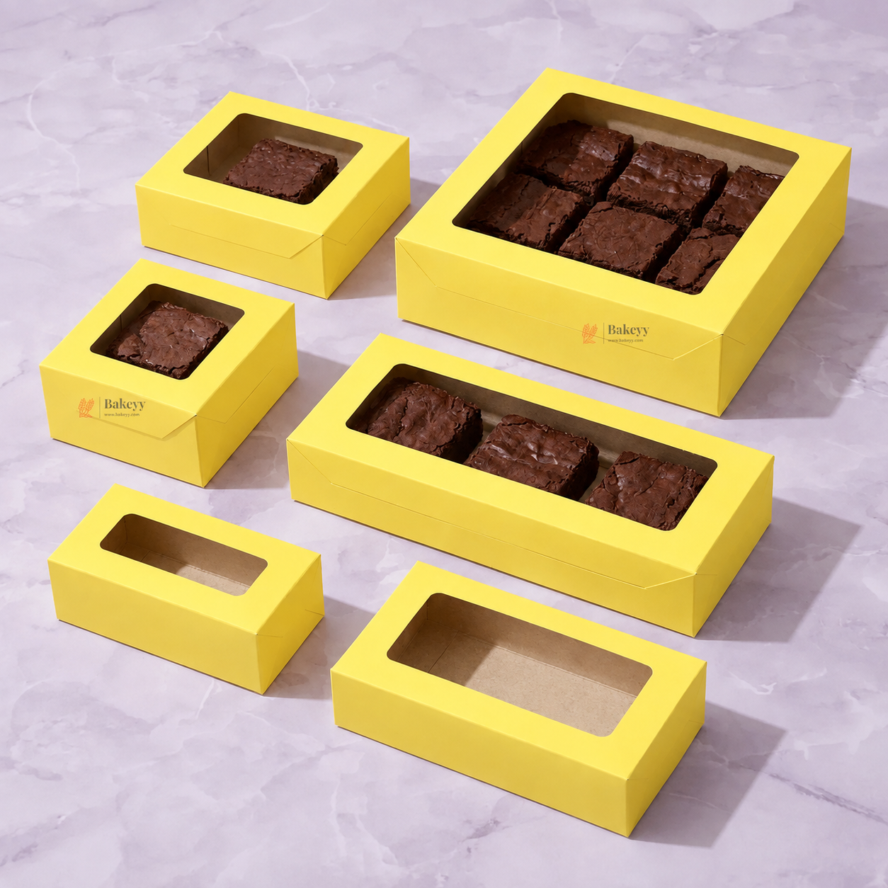 Six yellow bakery boxes in different sizes and shapes, some filled with brownies and one empty, arranged on a light purple marble surface. The boxes have clear window tops and a small 'Bake's' logo on the front.