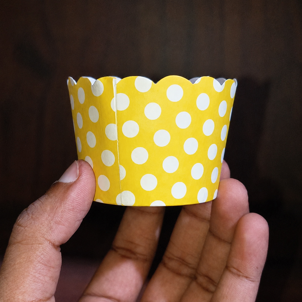 Yellow cupcake liner with white polka dots held in a hand against a dark background