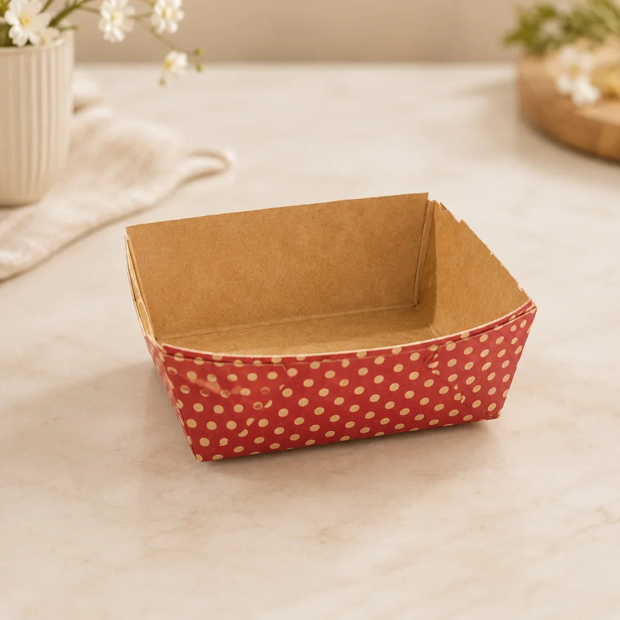Square paper basket with red and white polka dot pattern on a light surface.