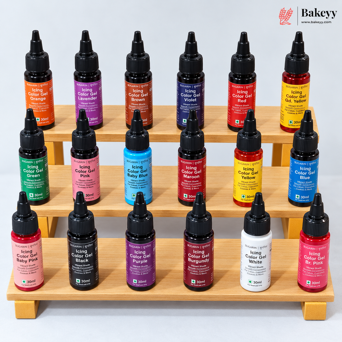 A set of 20 Bakey's brand icing color gel bottles in various vibrant colors, arranged neatly on a light-colored wooden tiered display stand against a clean white background.