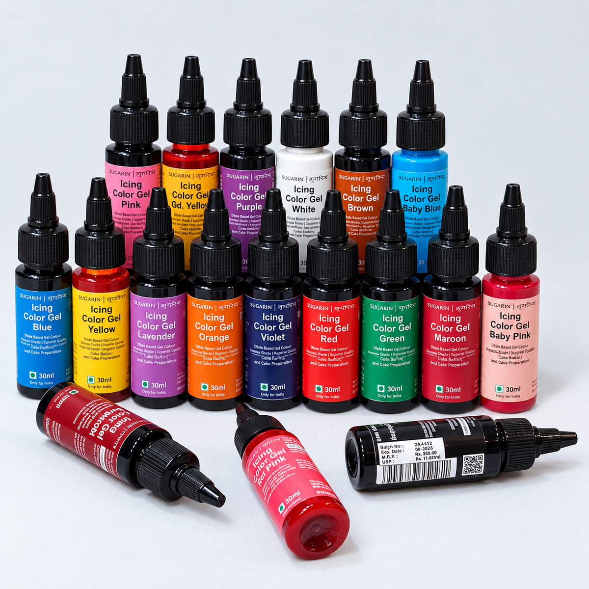 A set of small bottles of Royal Pro icing color gel, arranged in rows on a light gray background, with three bottles lying on their sides in front. The bottles contain various colored gel and are labeled with names like Blue, Yellow, Purple, White, Brown, Baby Blue, Red, Green, Maroon, Pink, and Lavender.
