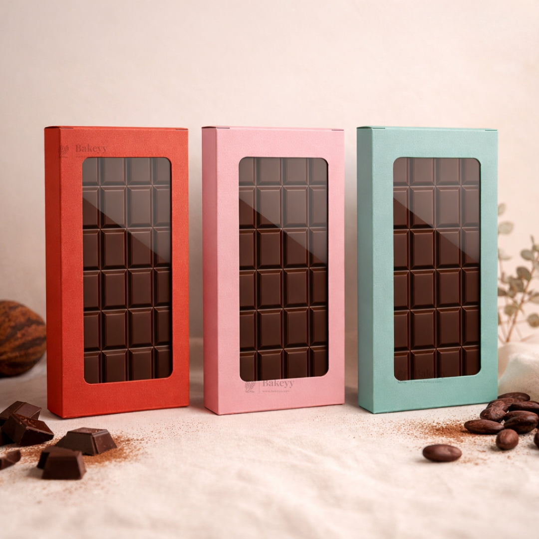 Three chocolate bars in colorful boxes on a light surface with cocoa beans.