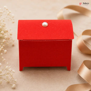Red gift box with a pearl on top, surrounded by ribbons and flowers on a beige background