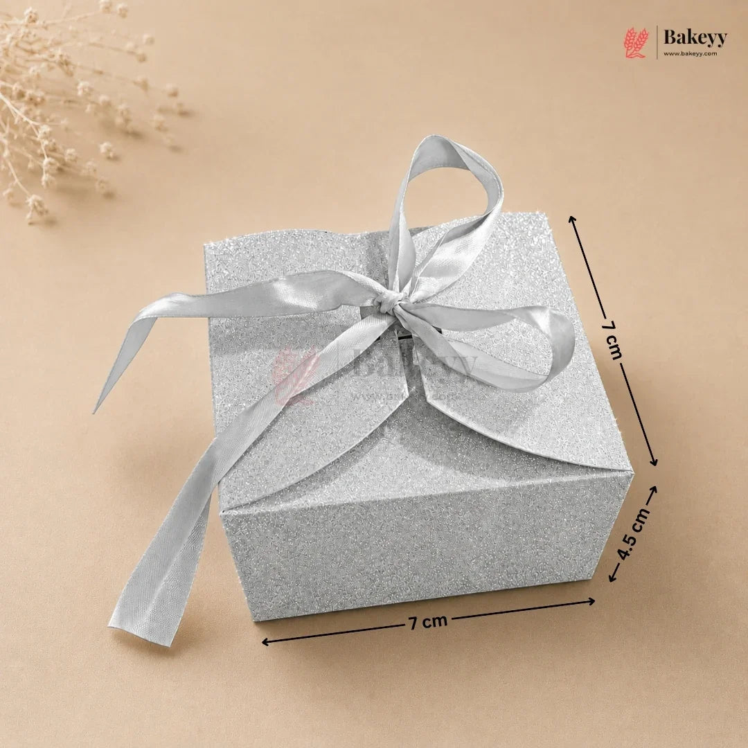 Silver gift box with a ribbon on a beige background, featuring dimensions.