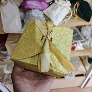 Gold glittery gift box with a ribbon held in front of shelves with various items.