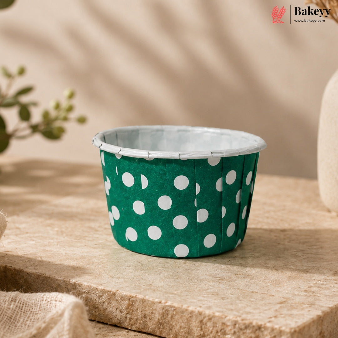 Green cupcake liner with white polka dots on a wooden surface, featuring the Bakey brand.