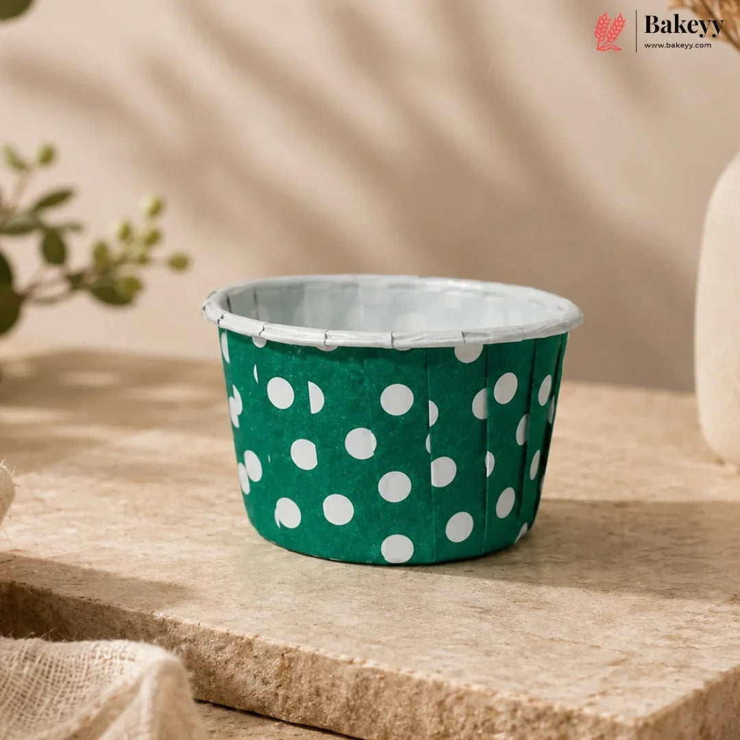 Green cupcake liner with white polka dots on a wooden surface, featuring the Bakey brand.