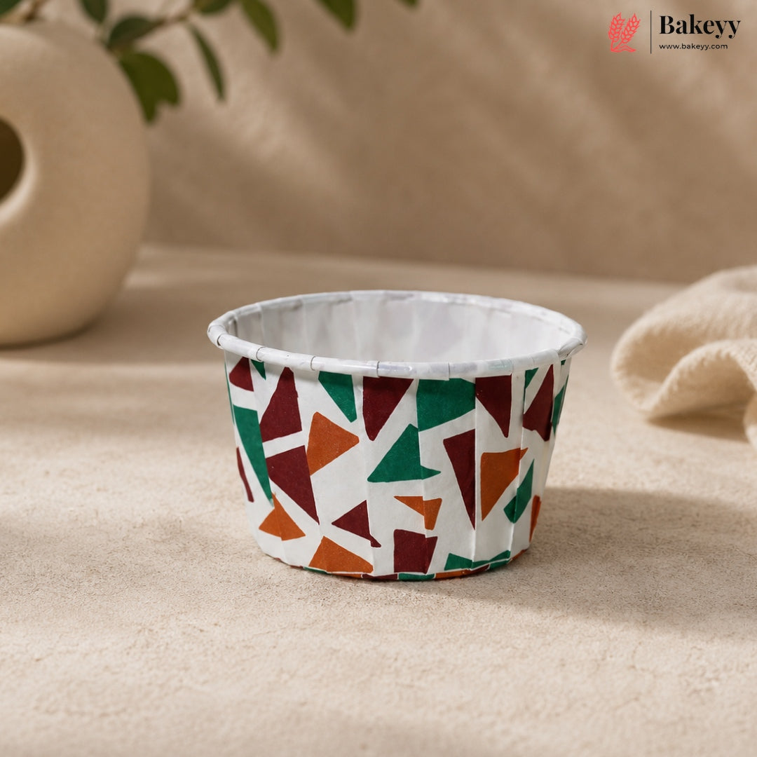 Colorful geometric-patterned cupcake liner on a beige surface with 'Bakeyy' branding.