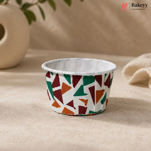 Colorful geometric-patterned cupcake liner on a beige surface with 'Bakeyy' branding.