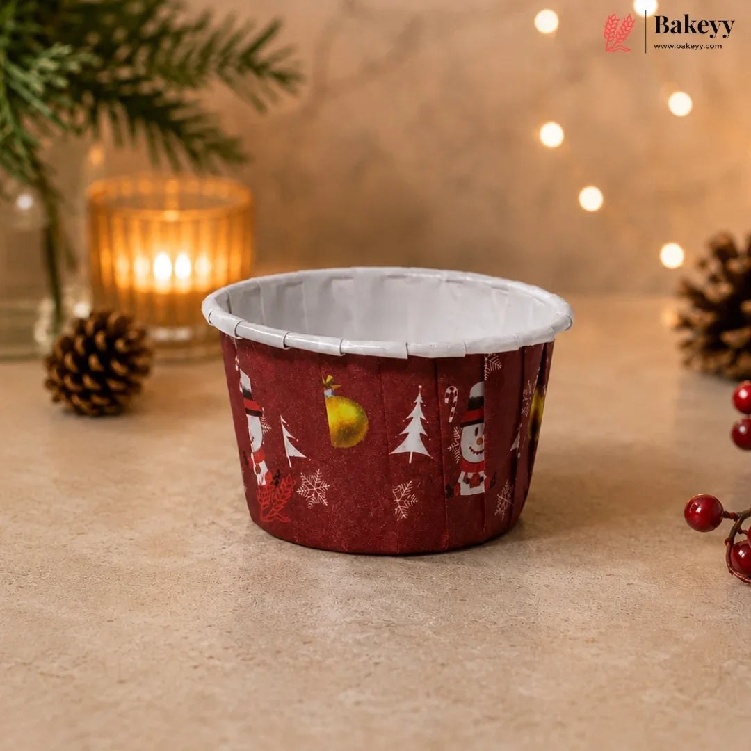 Red cupcake liner with Christmas patterns on a wooden surface with decorative lights and pine cones.
