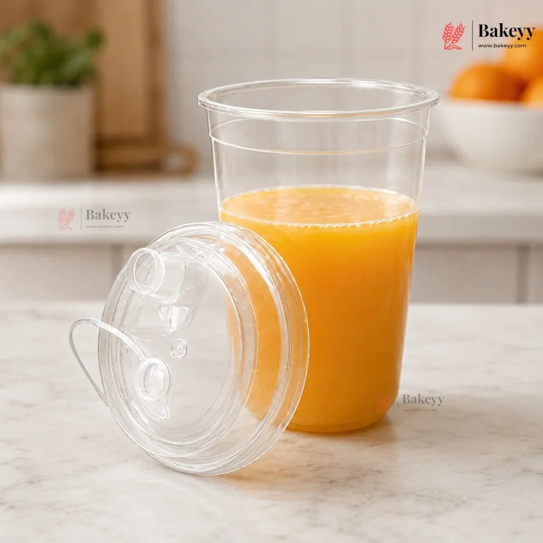 Clear plastic cup with orange juice and lid on a light surface, with Bakeyy branding.