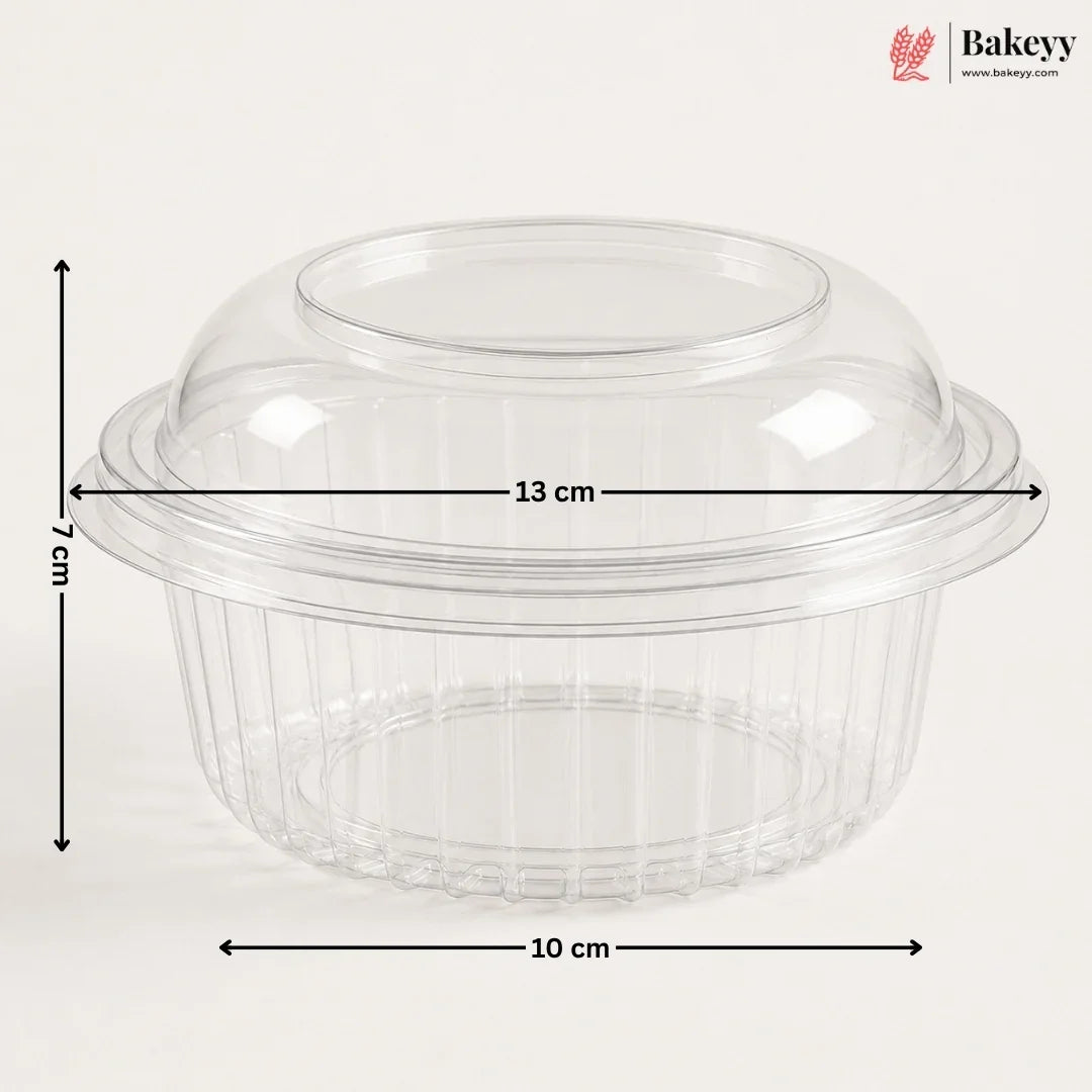 Clear plastic dome lid with a flared rim and ribbed base, shown with dimension arrows and labels indicating 13 cm width, 10 cm base diameter, and 7 cm height on a light gray background. Bakeyy logo appears in the top right.