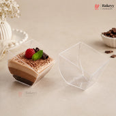 Two clear plastic dessert cups on a beige surface, with one cup filled with a layered chocolate dessert topped with a raspberry and mint, and the other cup shown empty.