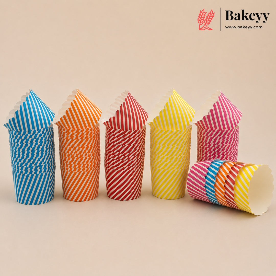 Six stacks of paper cupcake liners in assorted colors and stripe patterns, including blue and white, orange and white, red and white, yellow and white, pink and white, and a multicolor stack lying on its side. The Bakeyy brand logo is visible in the top right corner against a solid beige background.