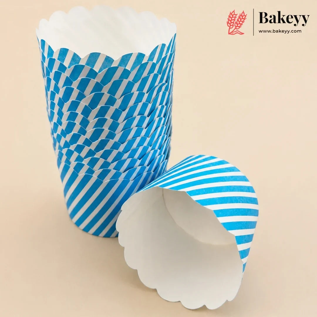 Blue and white striped paper cupcake liners, with one liner standing upright and another lying on its side to show the white scalloped inner lining, on a beige background. A Bakeyy brand logo is visible in the top right corner.