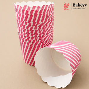 A stack of pink and white striped scalloped paper cupcake liners with one liner lying open in the foreground on a beige background. The Bakeyy logo is visible in the top right corner.