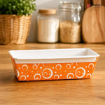 Rectangular baking dish with orange and white pattern on a wooden surface, branded 'Bakeyy'.