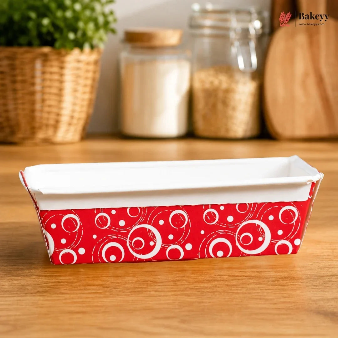 Rectangular baking dish with red and white pattern on a wooden surface, with jars and a plant in the background.