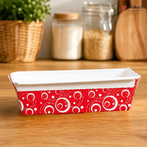 Rectangular baking dish with red and white pattern on a wooden surface, with jars and a plant in the background.