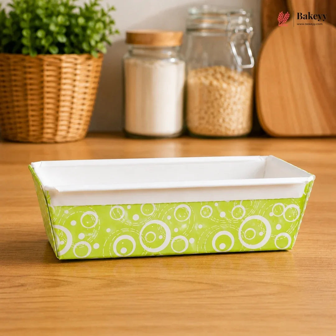 Rectangular baking dish with green and white pattern on a wooden surface, with jars and a plant in the background.