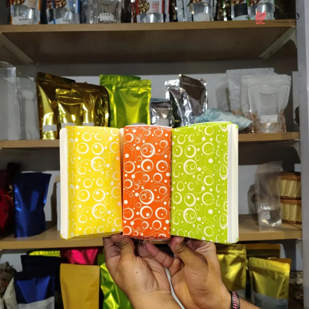 Three colorful packages with circular patterns held in front of a shelf with various other packages.