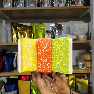 Three colorful packages with circular patterns held in front of a shelf with various other packages.