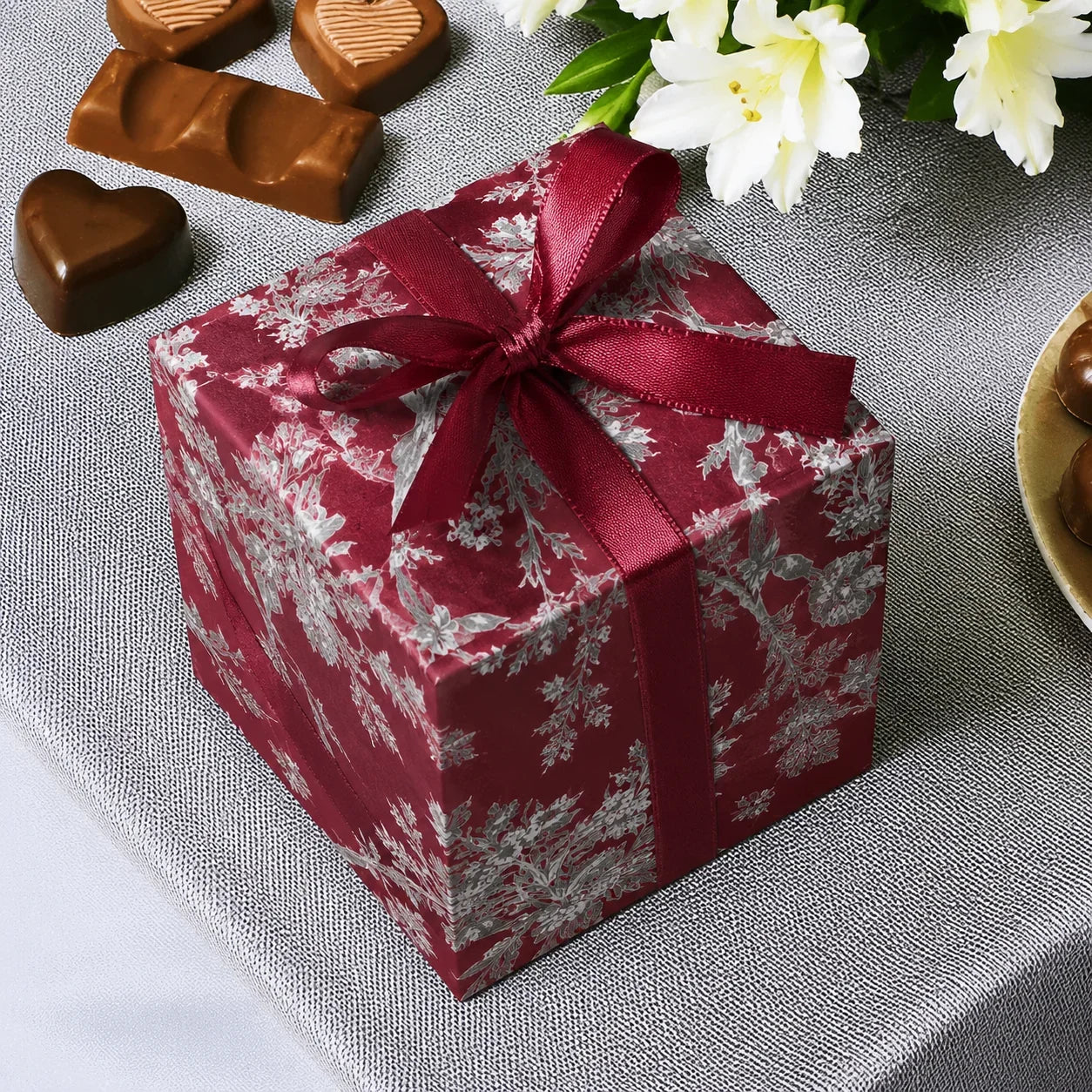Gift box with red ribbon on a gray surface with chocolates and flowers