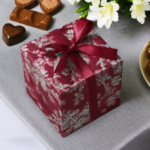 Gift box with red ribbon on a gray surface with chocolates and flowers