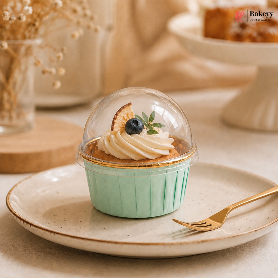 Cupcake in a green case with a clear dome on a plate, featuring the Bakey brand.