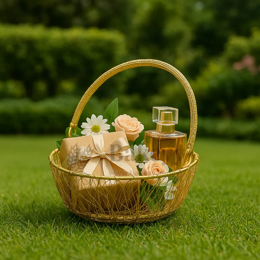 Gold hamper basket with perfume, a gift box, and faux flowers on green grass, Bakeyy gift packaging.