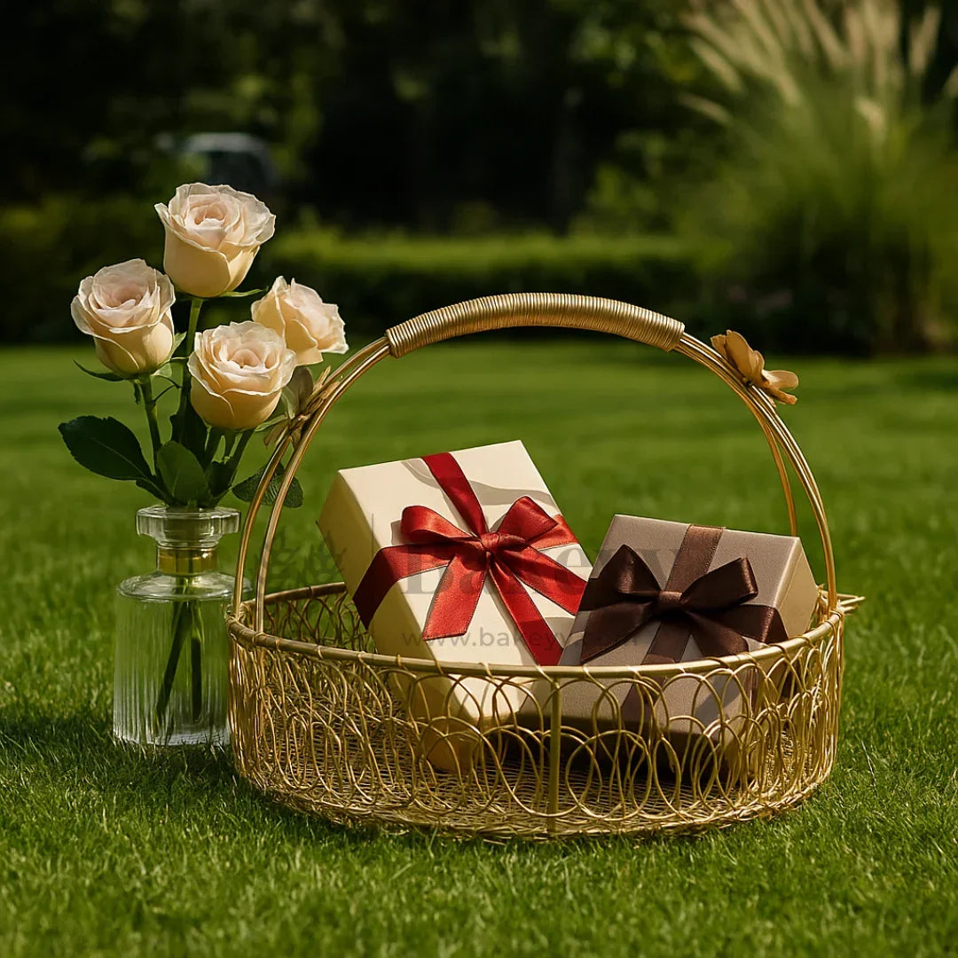 Gift hamper basket with ribbon-wrapped boxes and a vase of roses on green grass, Bakeyy.com