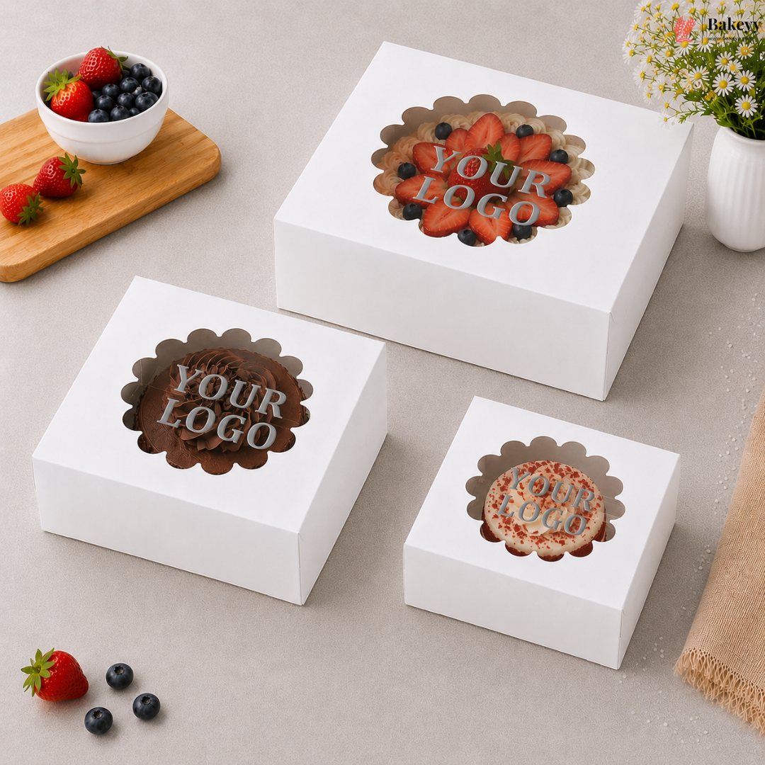 Three white cake boxes with a window on top, featuring a decorative logo and 'Your Logo' text, on a light gray surface.