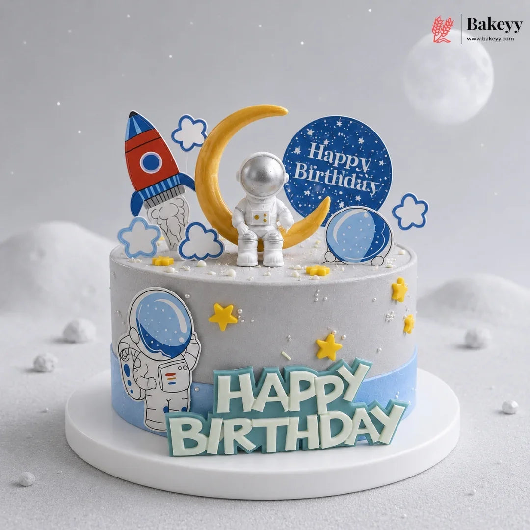 Space-themed birthday cake with astronaut, rocket, and moon decorations on a light gray background.