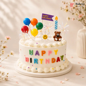 Birthday cake with colorful balloons, teddy bear, and candles on a light background