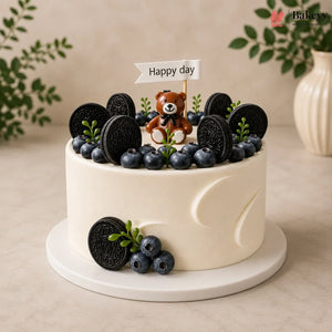 White cake with blueberries, Oreo cookies, and a teddy bear on top with 'Happy day' sign.