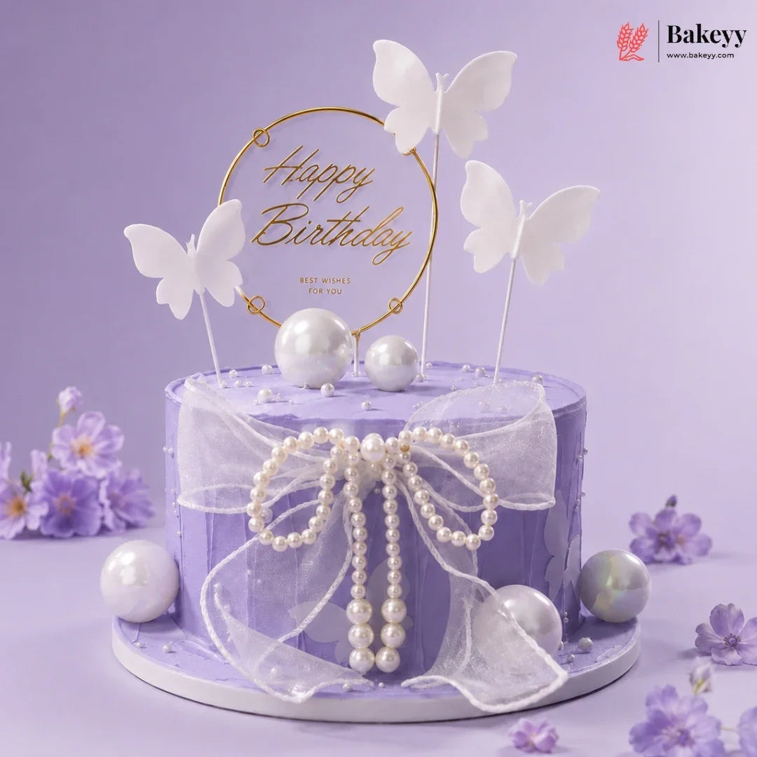 Purple birthday cake with butterfly toppers and pearl decorations on a purple background, featuring the Bakeyy brand.