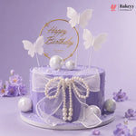 Purple birthday cake with butterfly toppers and pearl decorations on a purple background, featuring the Bakeyy brand.