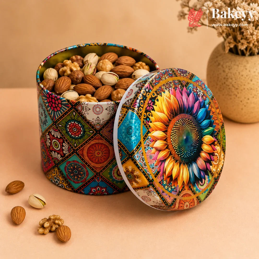 A round metal tin filled with assorted nuts and dried fruits, shown with its lid leaning against the side. The tin has a colorful geometric pattern on the body and a large sunflower design on the lid.