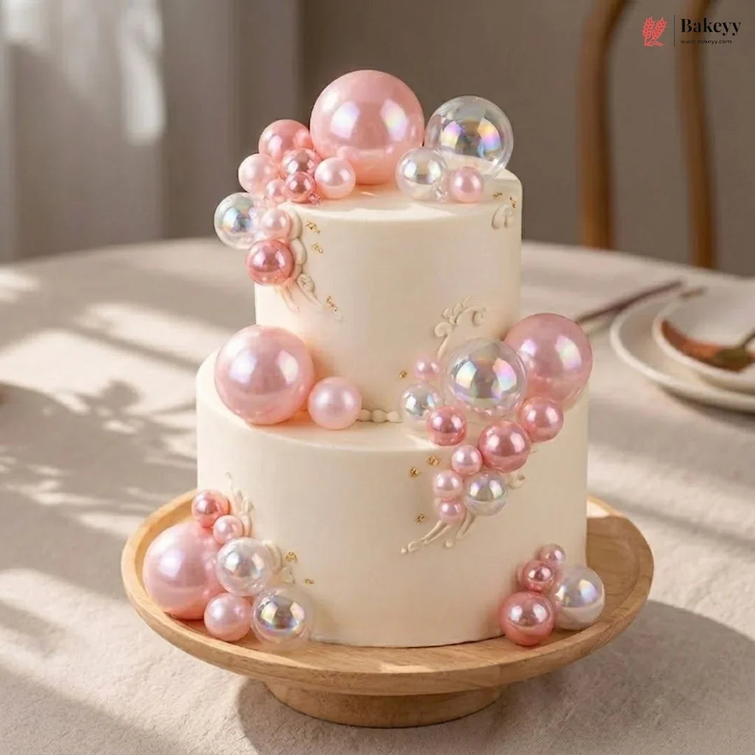 Two-tier cake decorated with pink and clear balloons on a wooden stand.