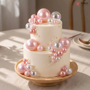 Two-tier cake decorated with pink and clear balloons on a wooden stand.