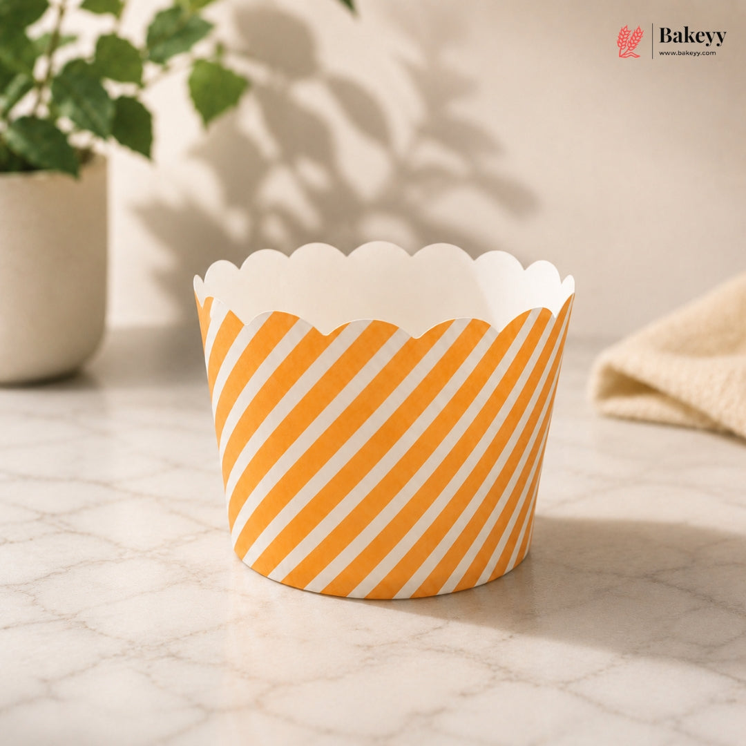 Orange and white striped paper cupcake liner on a marble surface with a plant in the background.