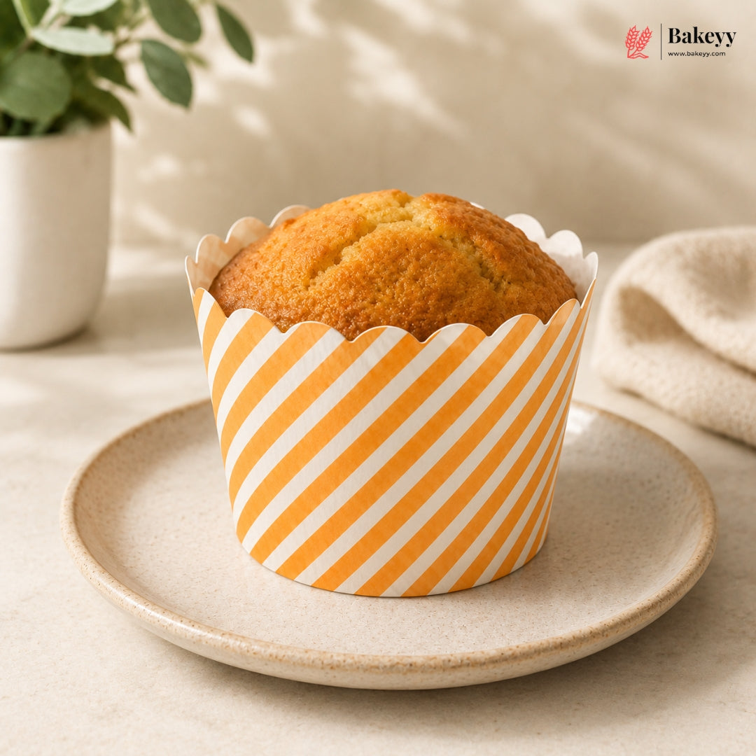 Muffin in a striped paper cup on a plate with a plant and towel in the background