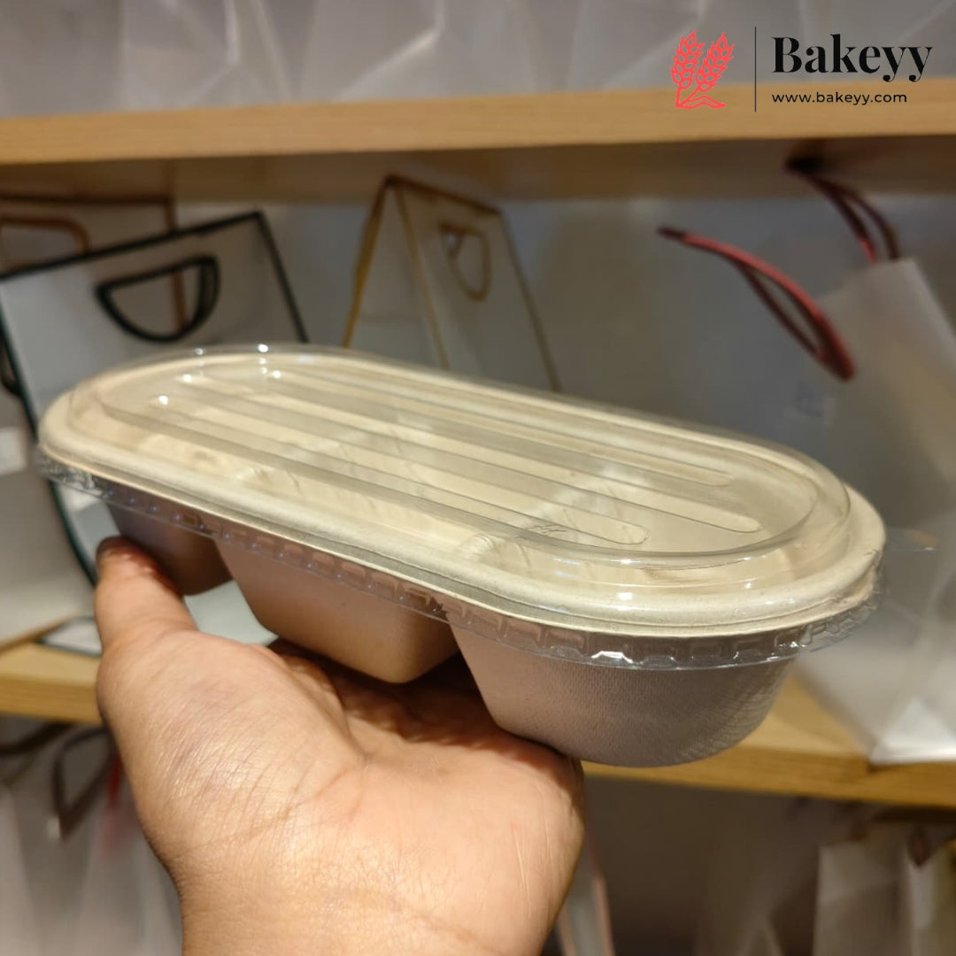 A hand holding a two-compartment biodegradable paper tray with a clear plastic lid, set against a blurred background of shelves and packaging.