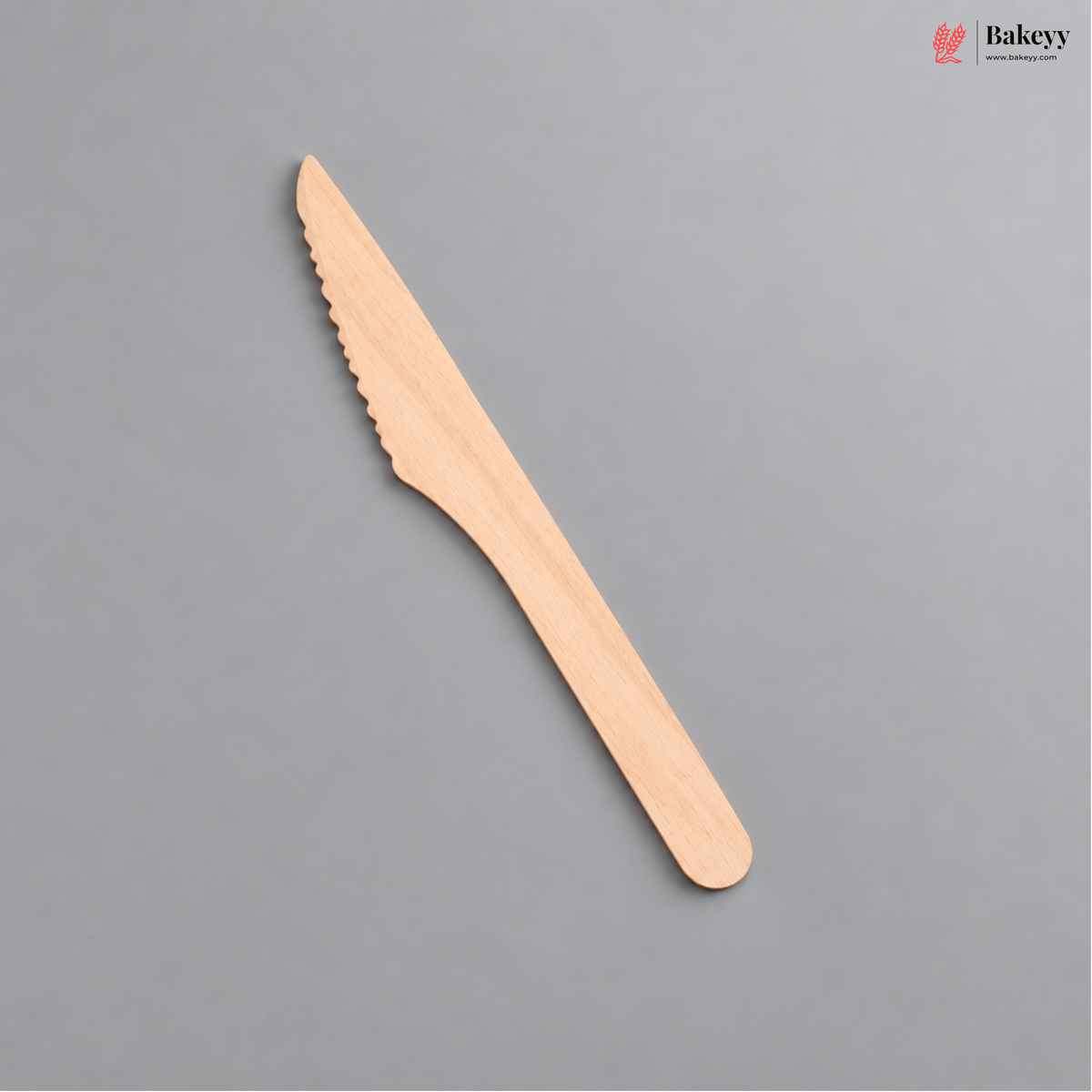 A single wooden cake server with a serrated blade, shown diagonally on a solid gray background. The Bakeyy logo is visible in the top right corner.