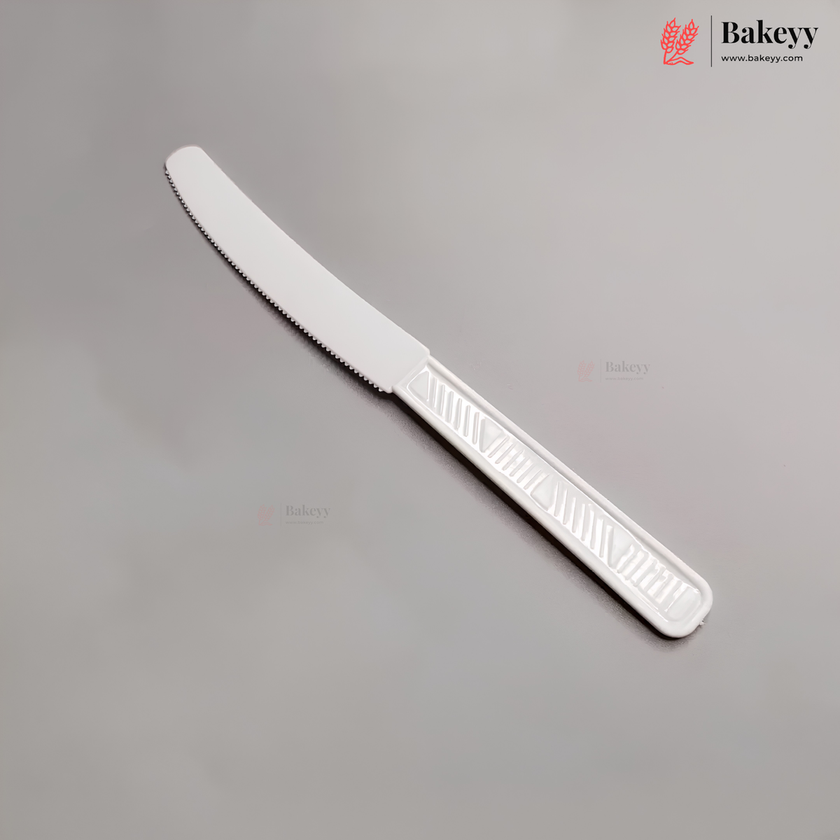 A white plastic serving knife with a serrated blade, shown diagonally on a neutral gray background with Bakeyy branding.