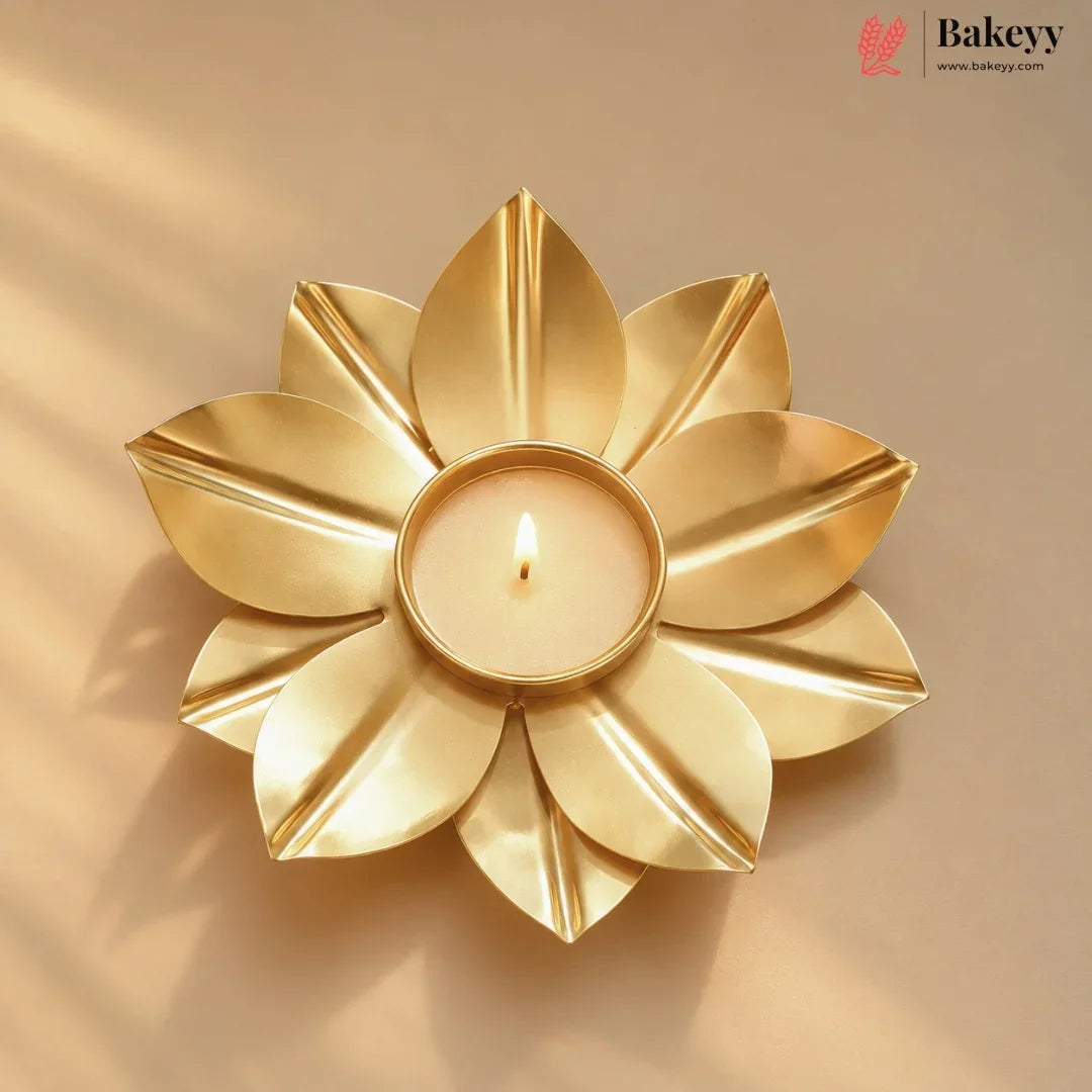 A gold-toned flower-shaped candle holder with a lit tealight candle in the center, set against a warm beige background with soft shadows. The Bakeyy logo is visible in the top right corner.